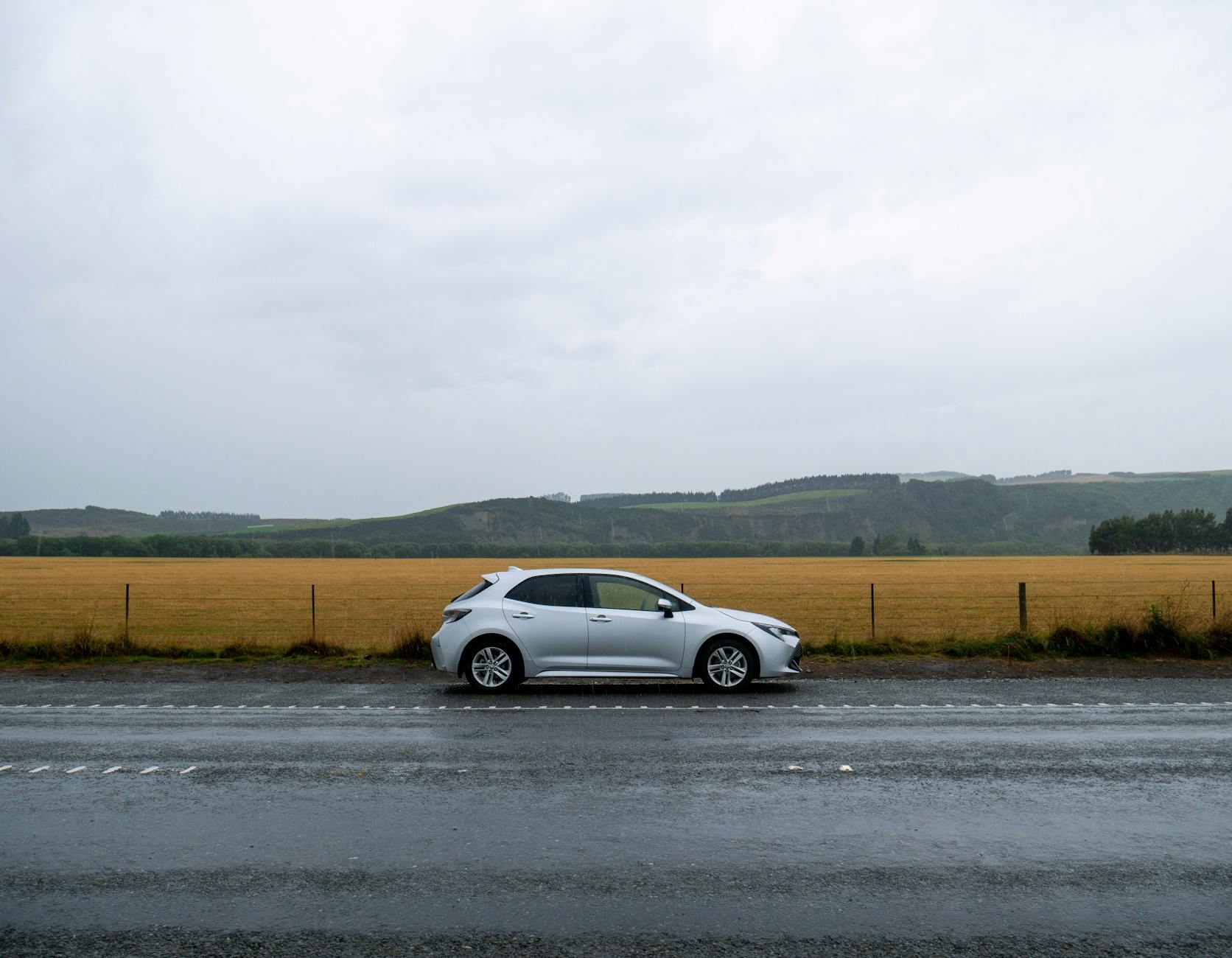 Srebrny Mercedes klasy E zaparkowany na mokrej drodze przy polu siana
