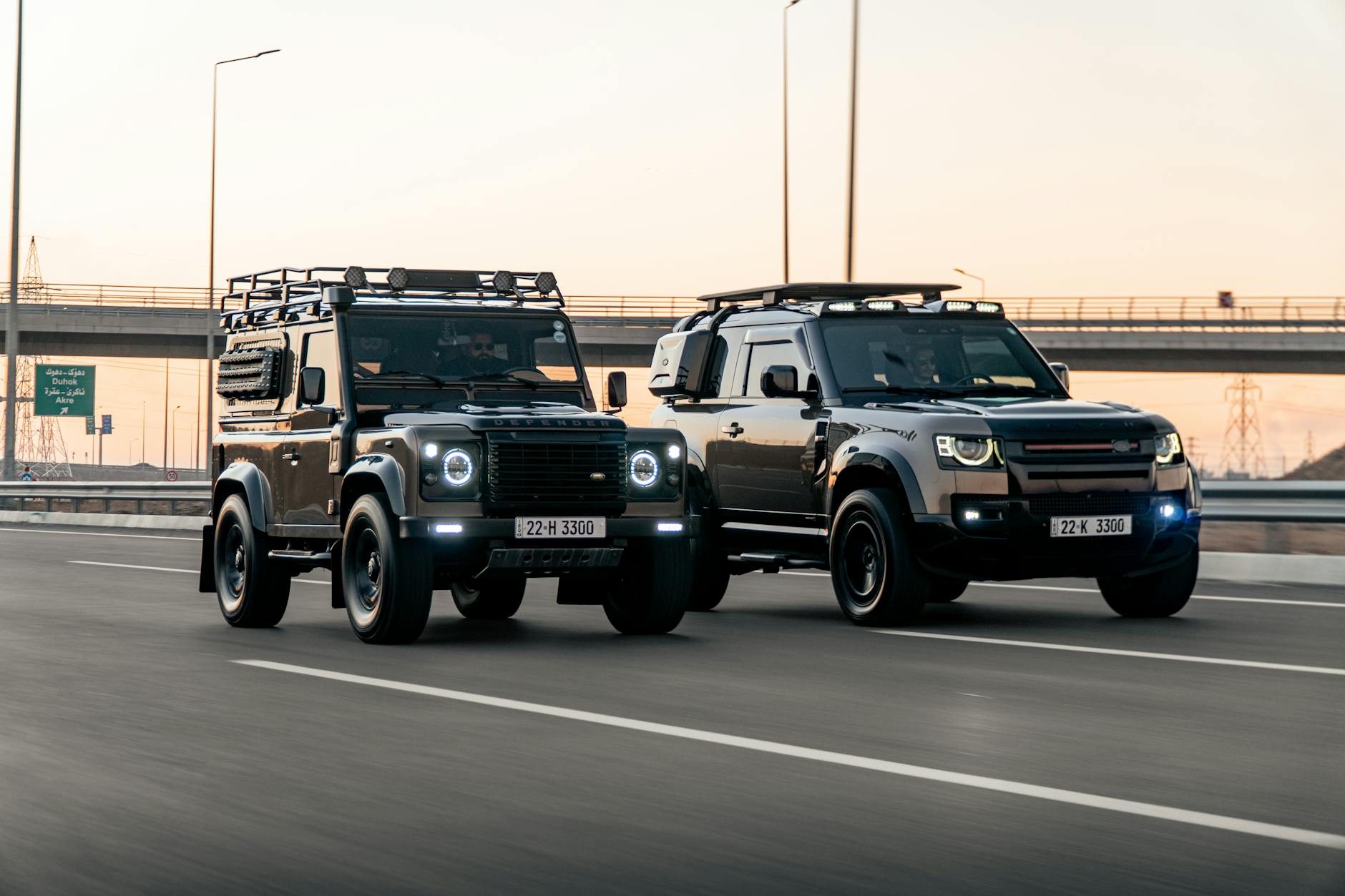 Dwa terenowe SUV-y jadą równolegle autostradą o zachodzie słońca