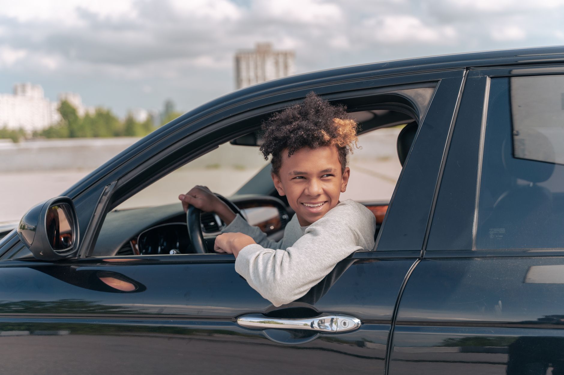 Czy Tesla nadaje się na pierwsze auto miejskie kierowcy Młody kierowca uśmiecha się, siedząc w samochodzie w słoneczny dzień