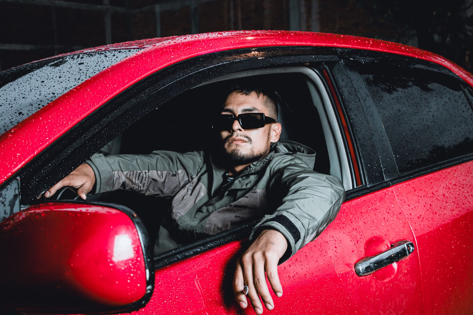 Młody kierowca w czerwonym BMW nocą w deszczu